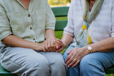 granddaughter consoling her senior grandmother and touching her hand when sitting on bench